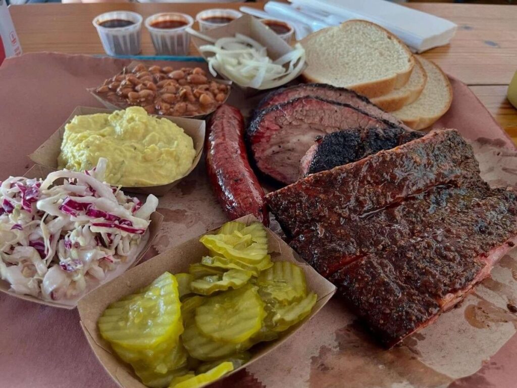 Tray of sliced brisket, ribs, and sides at a classic Texas barbecue spot in Austin