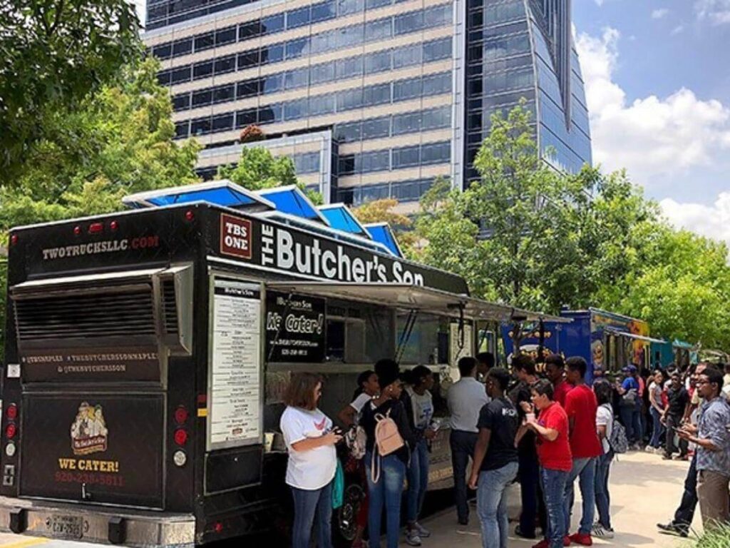 People relaxing on the lawn with food trucks in the background at Klyde Warren Park in Dallas