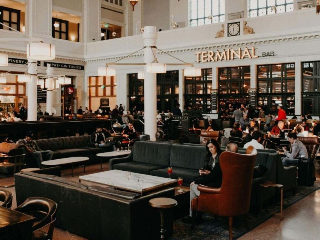People drinking coffee and working on laptops inside Union Station beneath tall windows and warm light