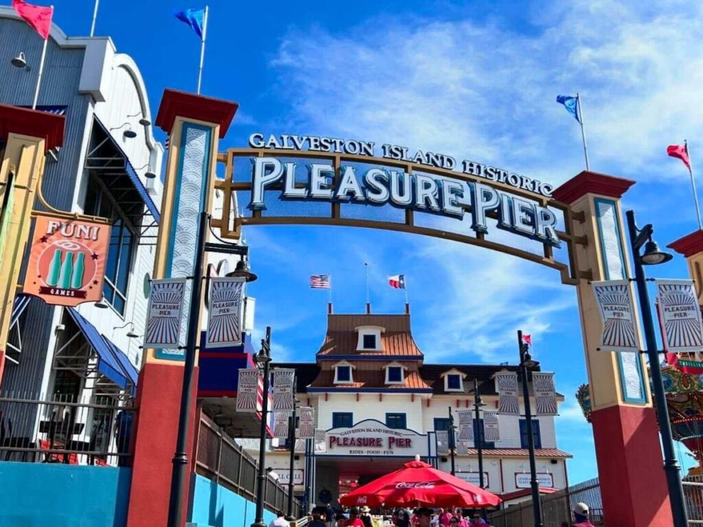 Colorful lights of Galveston’s Pleasure Pier reflecting over the water at sunset.