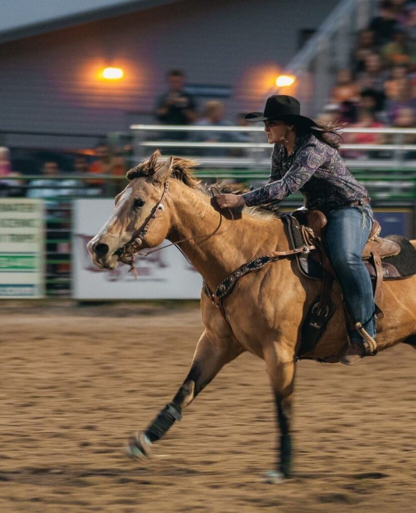 Cowgirl riding a bronco at Jackson Hole Rodeo under bright arena lights at night
