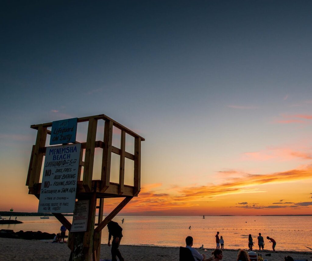 Spectacular sunset over Menemsha Beach with people gathered on the sand.