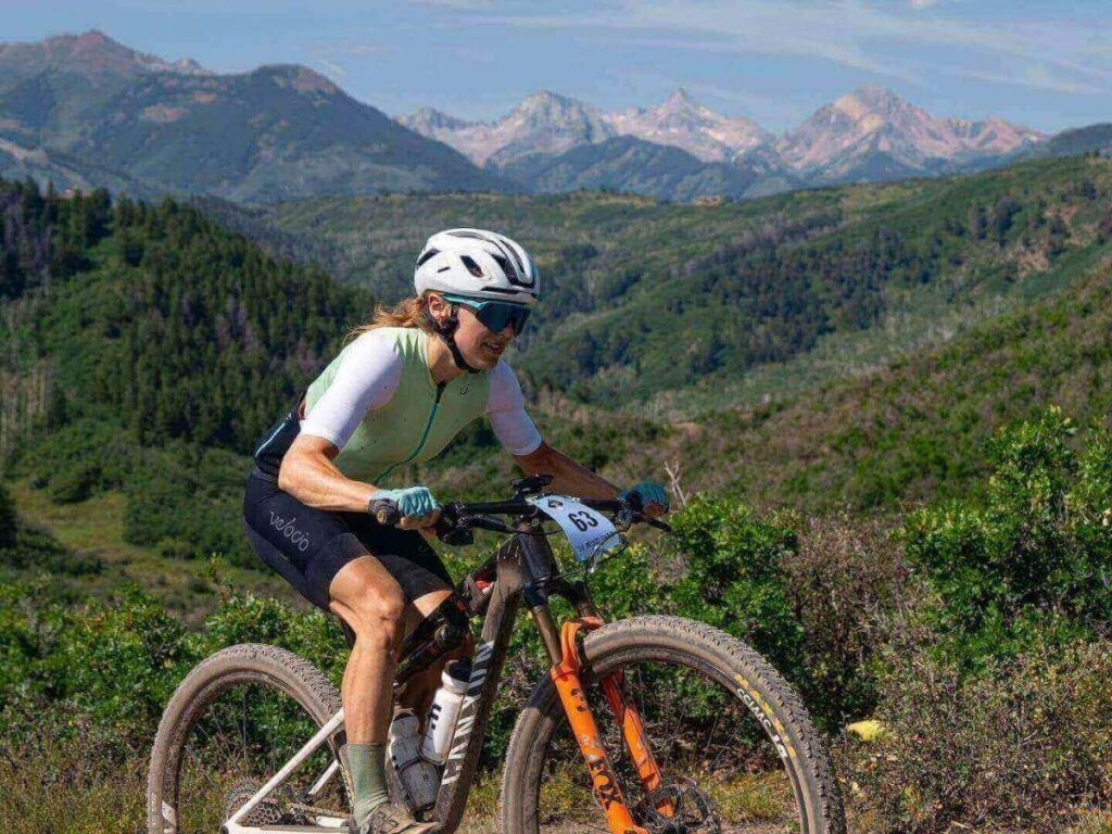 Mountain biker riding a dirt trail in Snowmass with grassy slopes and chairlifts in the distance