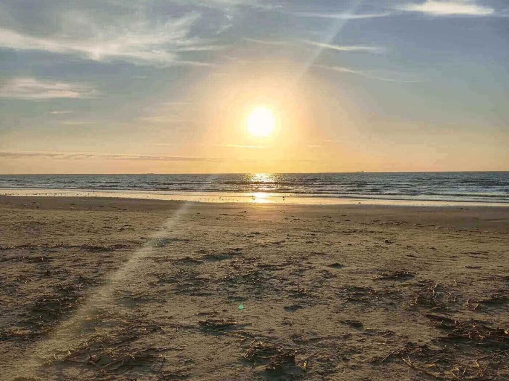 Wide sandy stretch of Stewart Beach with umbrellas, families, and gentle Gulf waves.