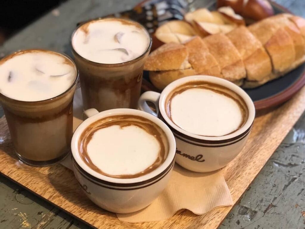 A person holding a coffee cup while walking along Carmel Beach in the early morning light