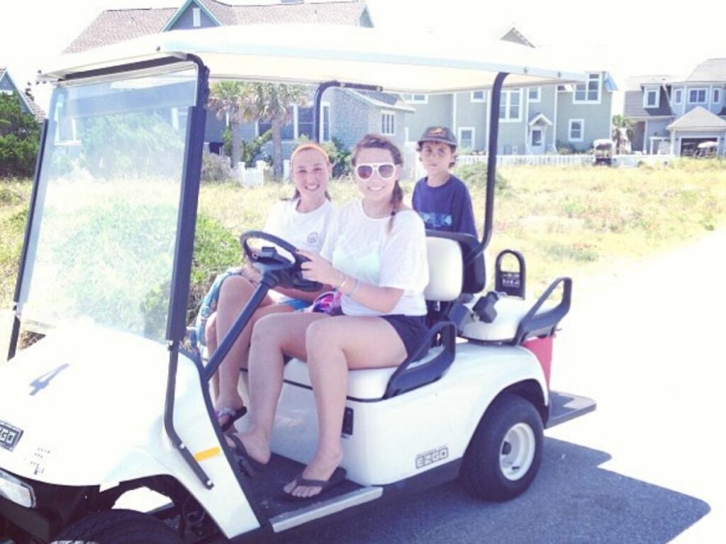 Electric golf cart driving down a shaded island lane under live oaks.