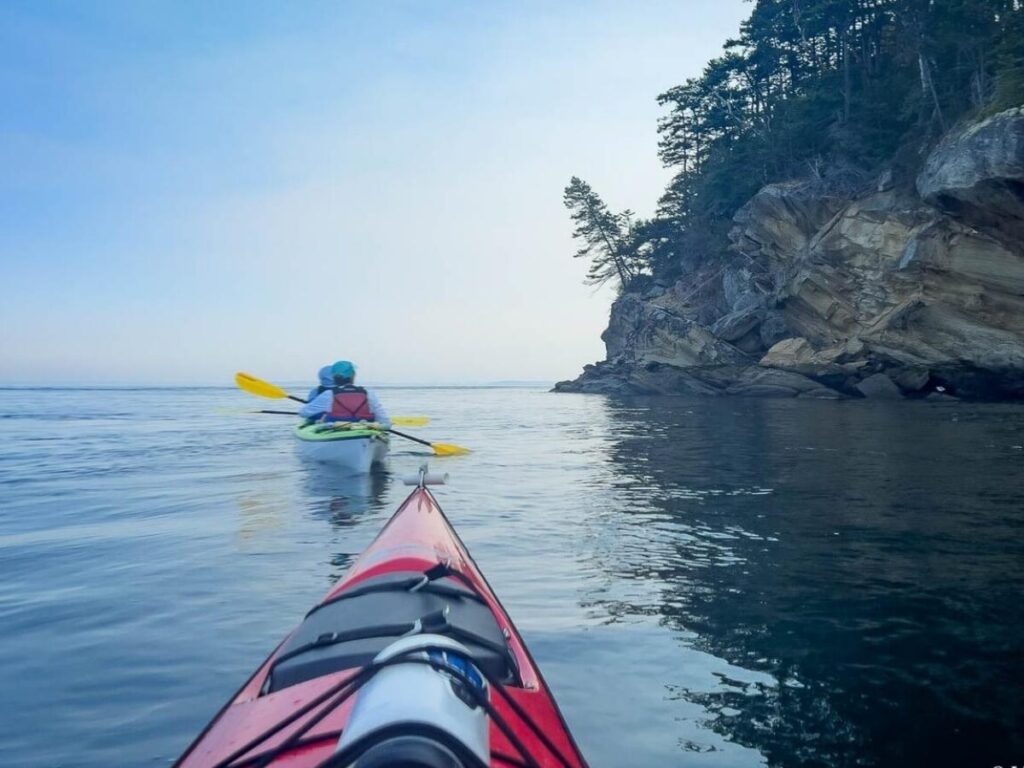 Kayakers paddling along the rocky coastline of the San Juan Islands