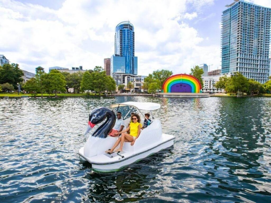 Swan boats floating on Lake Eola with people relaxing along the shore