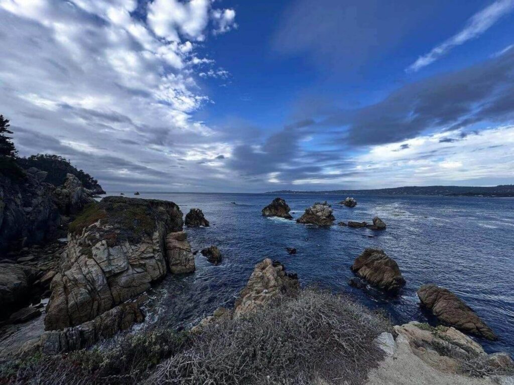 Rocky cove and wind-twisted cypress trees along the Point Lobos trail with turquoise water below.