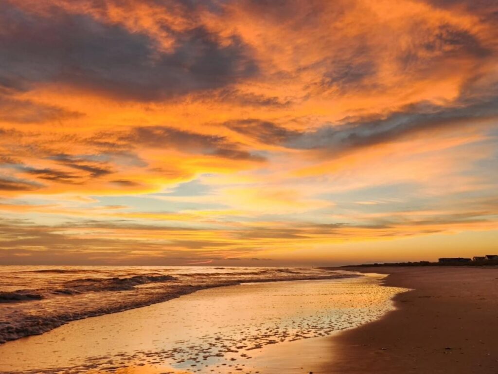 Sunset over West Beach with gentle waves and silhouetted figures.
