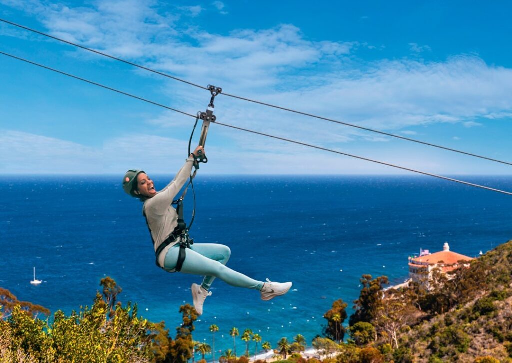 Adventurer mid-zipline across Descanso Canyon overlooking the ocean