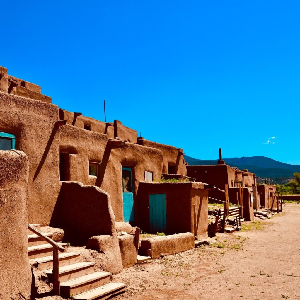 Adobe buildings of Taos Pueblo under morning light with mountains in the background