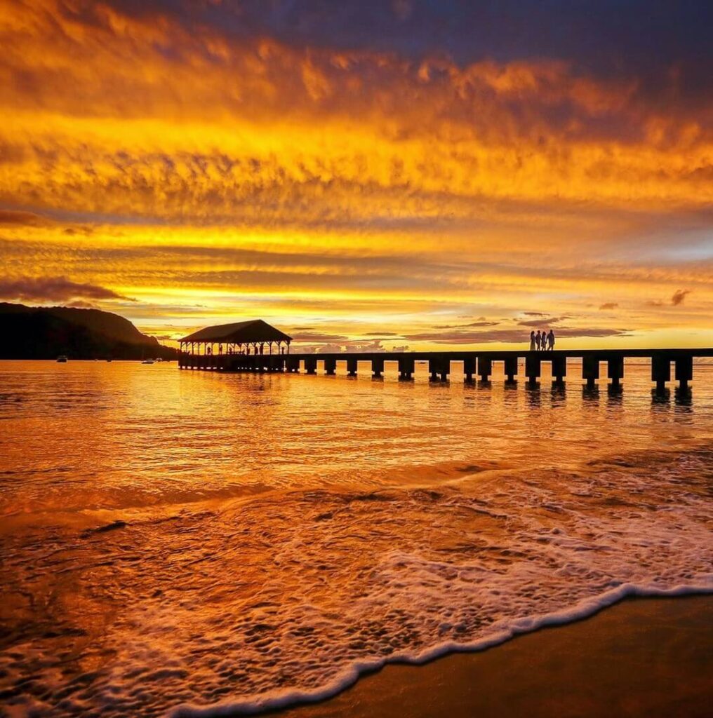 Hanalei Bay at sunset with paddleboarder and mountains in the distance