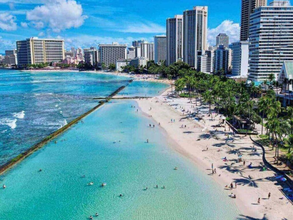 Calm morning water at Waikiki Beach with surfers and hotels in the background