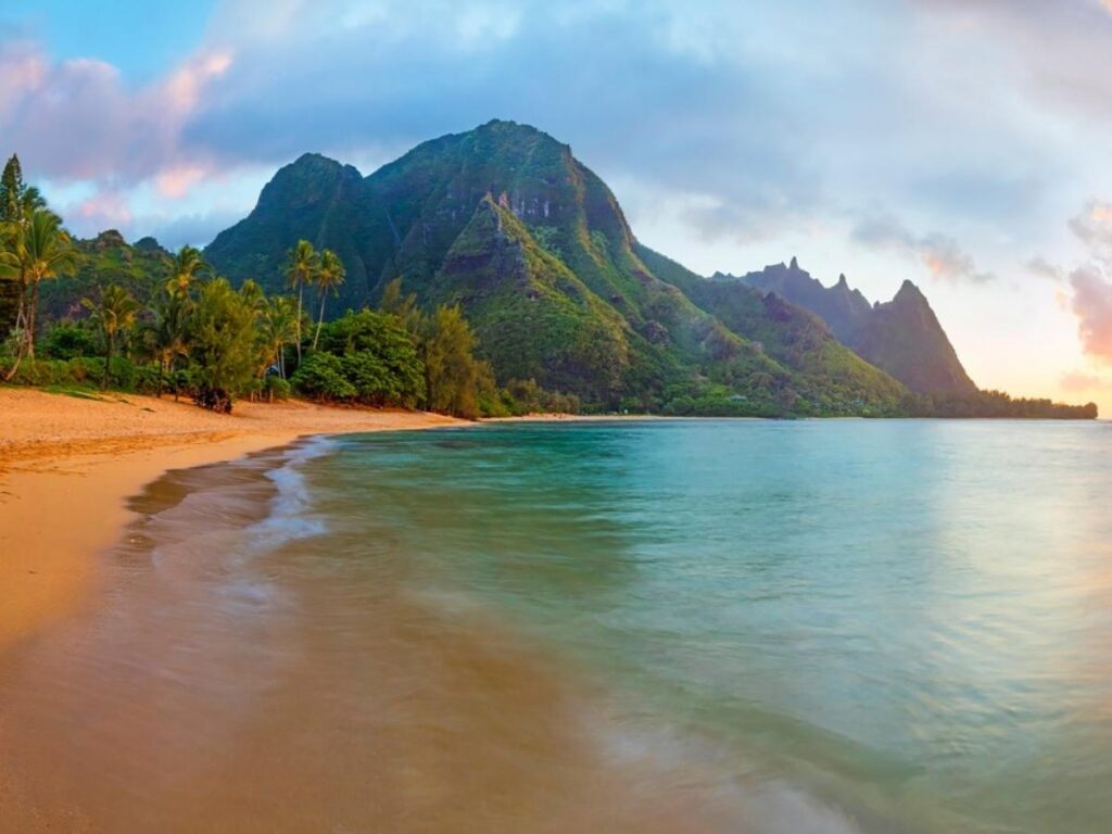 Calm beach at Hāʻena State Park with green cliffs in the background