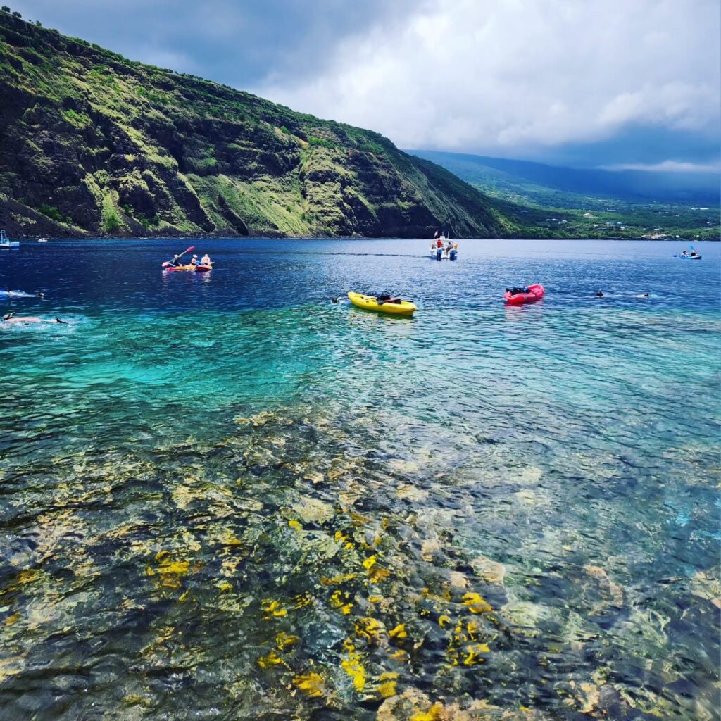Kayakers and snorkelers exploring calm waters at Kealakekua Bay near the Captain Cook Monument