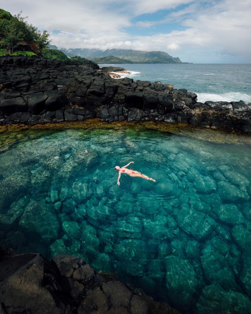 Lava rock tidepool at Queen’s Bath filled with clear water and ocean beyond