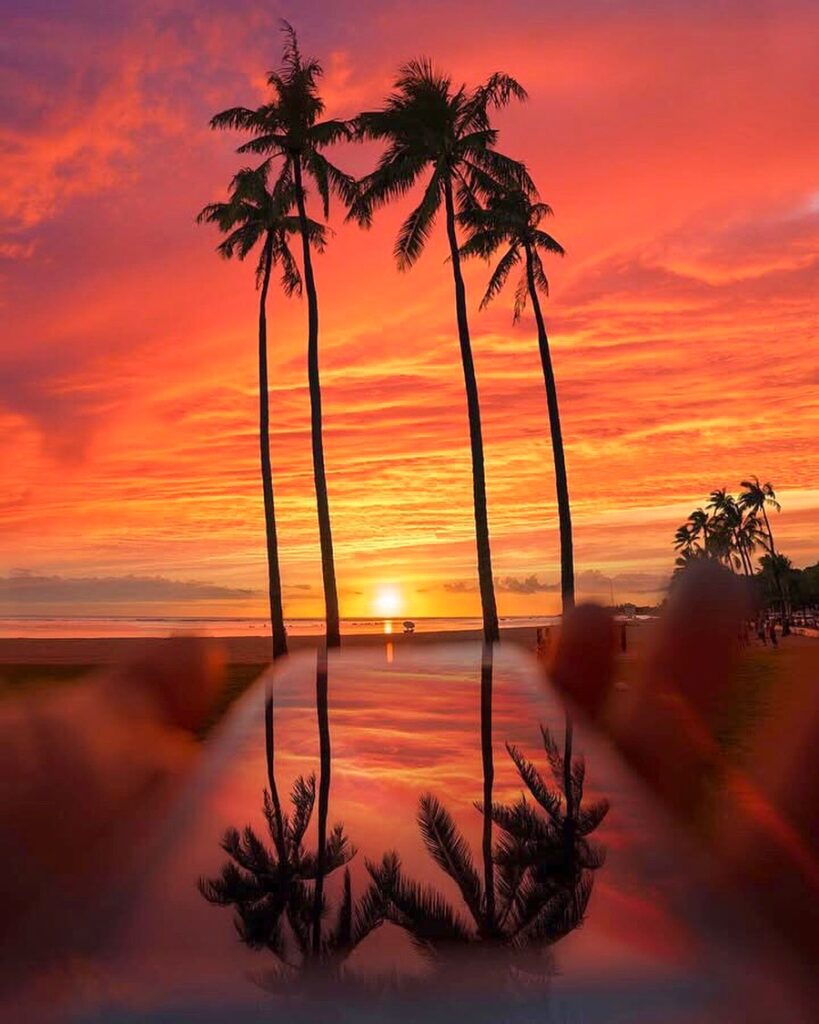 People relaxing on Waikiki Beach during sunset with surfers in the water