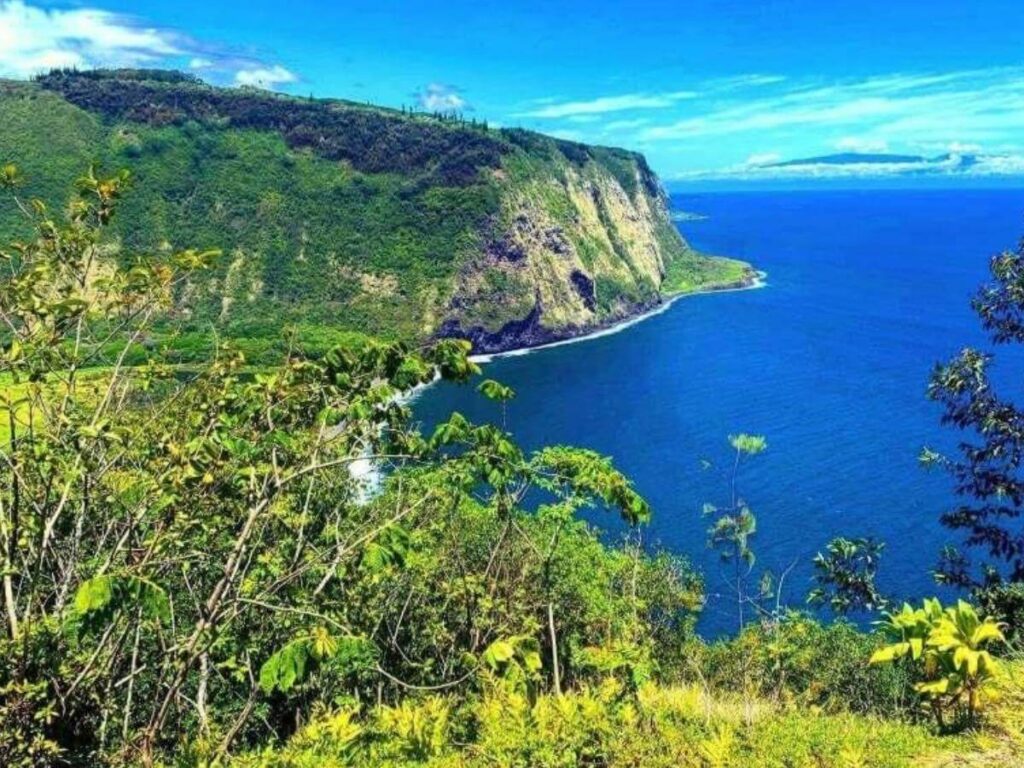 Late afternoon light over Waipio Valley cliffs and black sand beach