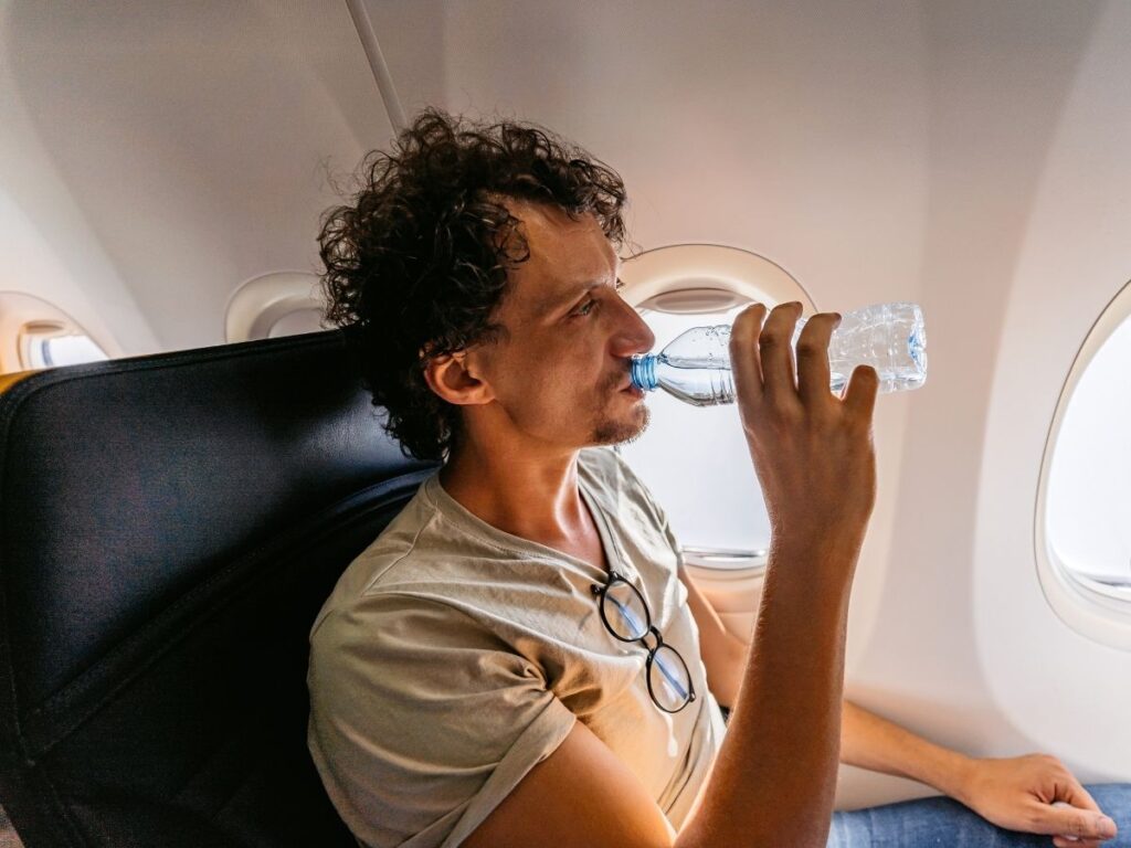 Traveler drinking water on an airplane next to a sunny window