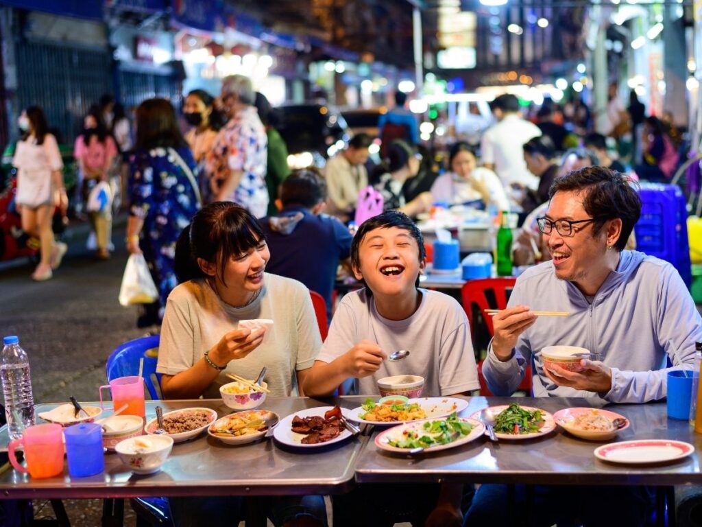hot plate of freshly grilled street food being served, with steam rising and locals in the background