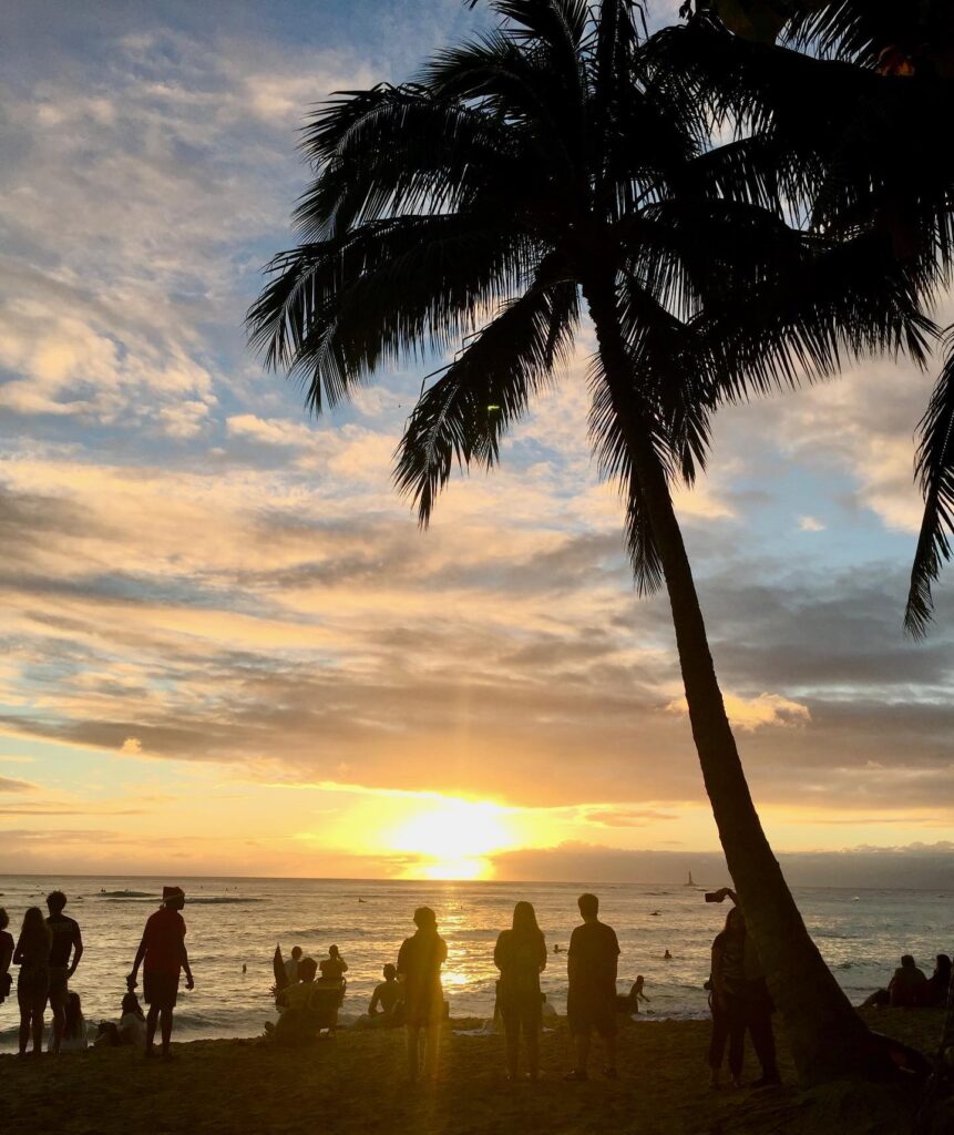 Sunset over Waikiki Beach with Diamond Head, palm trees, and surfers on Oahu