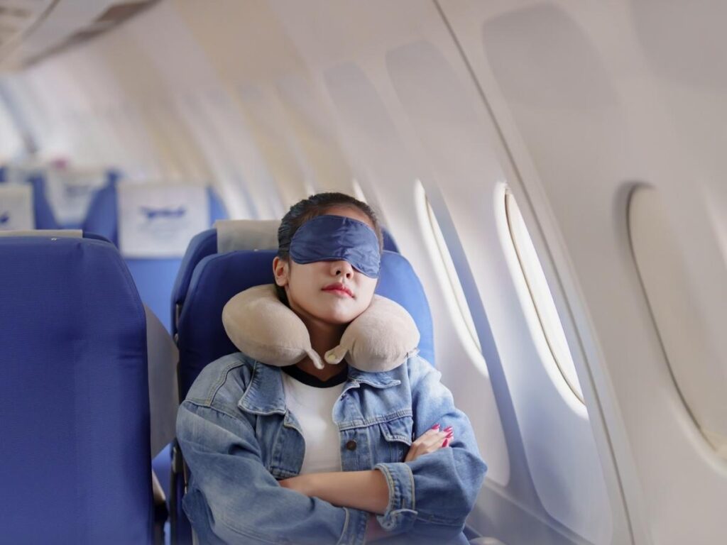 Traveler sleeping on airplane with neck pillow and eye mask.
