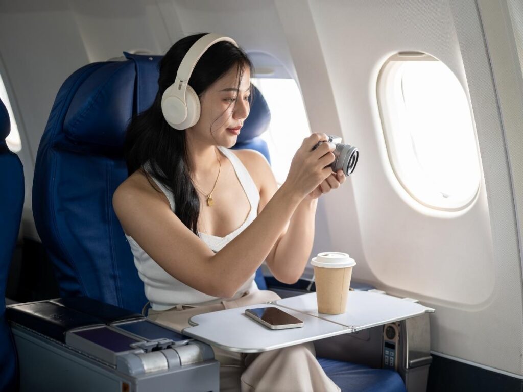 Traveler wearing noise-canceling headphones and looking out of an airplane window during cruise.