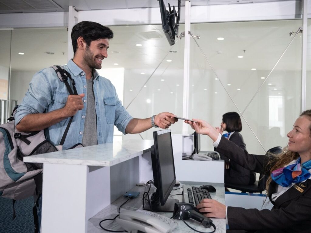 Airline counter agent handing a printed boarding pass to a traveler at check-in.