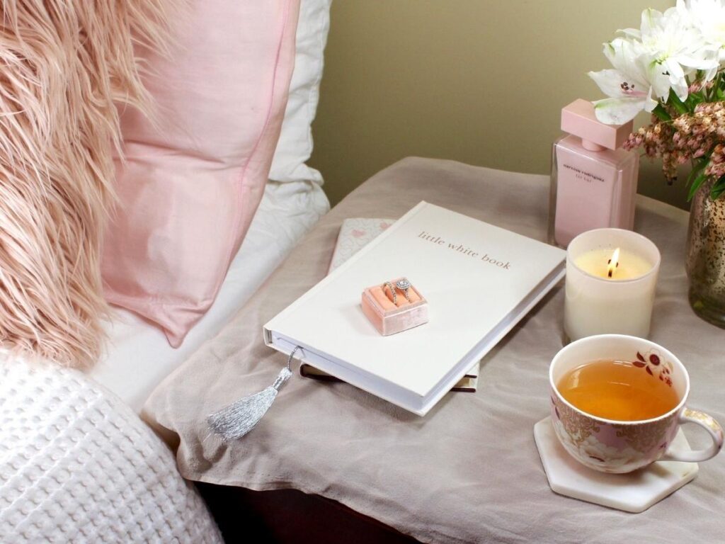 Bedside table with candle, perfume, and a small travel book.