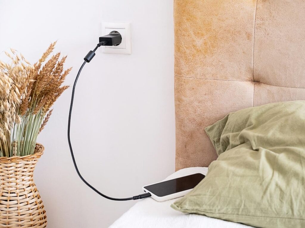 Guest testing an outlet by the nightstand with a phone charger plugged in.