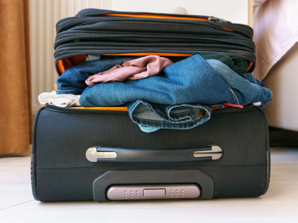 Carry-on bag overflowing with clothes on hotel floor