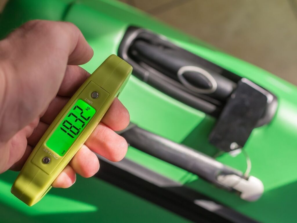Traveler using portable luggage scale to check bag weight.