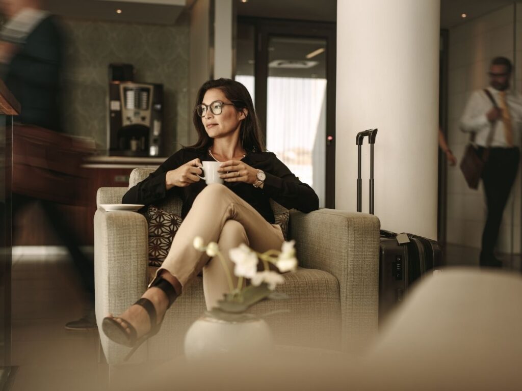 Solo female traveler seated in airport lounge with luggage and coffee