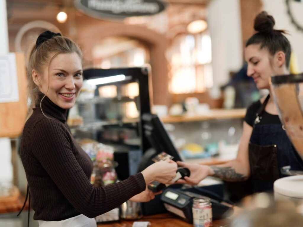 Traveler paying with a card reader at a European café, choosing local currency to avoid hidden conversion fees.