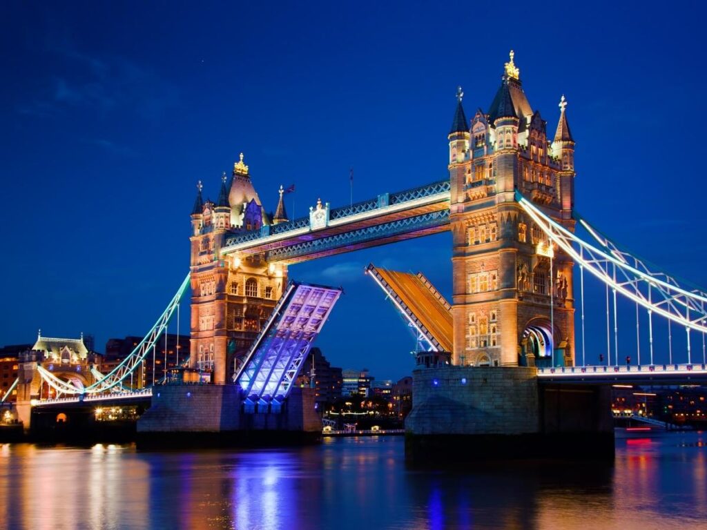 London’s Tower Bridge lit up at night with reflections on the River Thames.