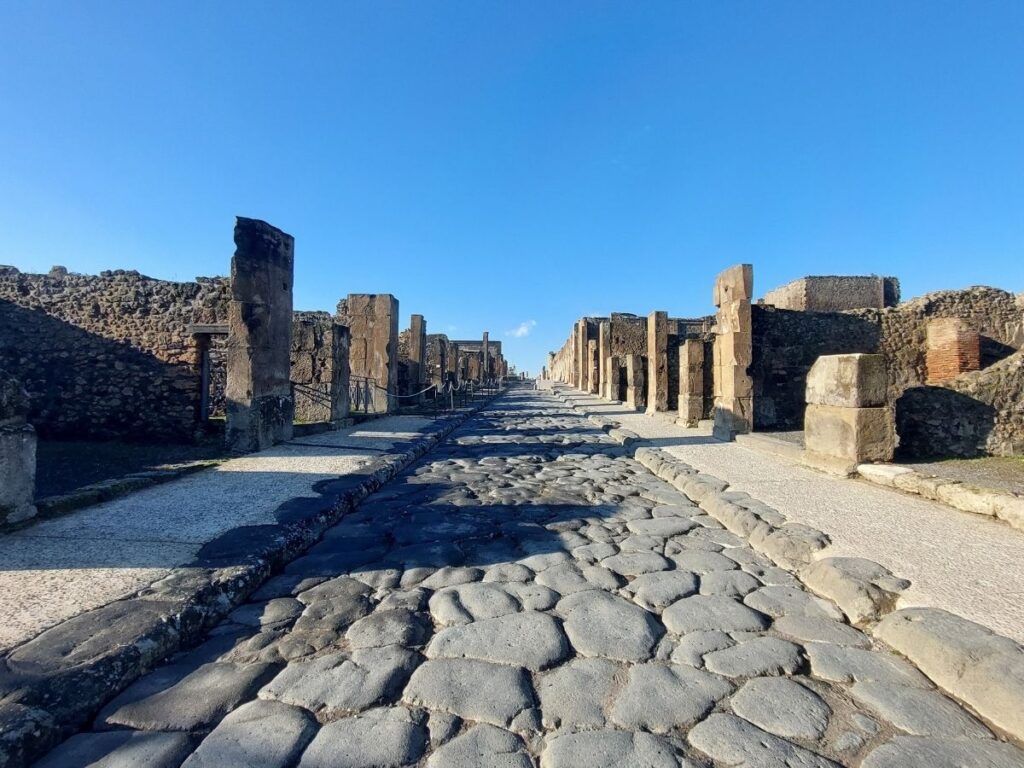 Ancient stone street of Via dell’Abbondanza lined with ruins in Pompeii.