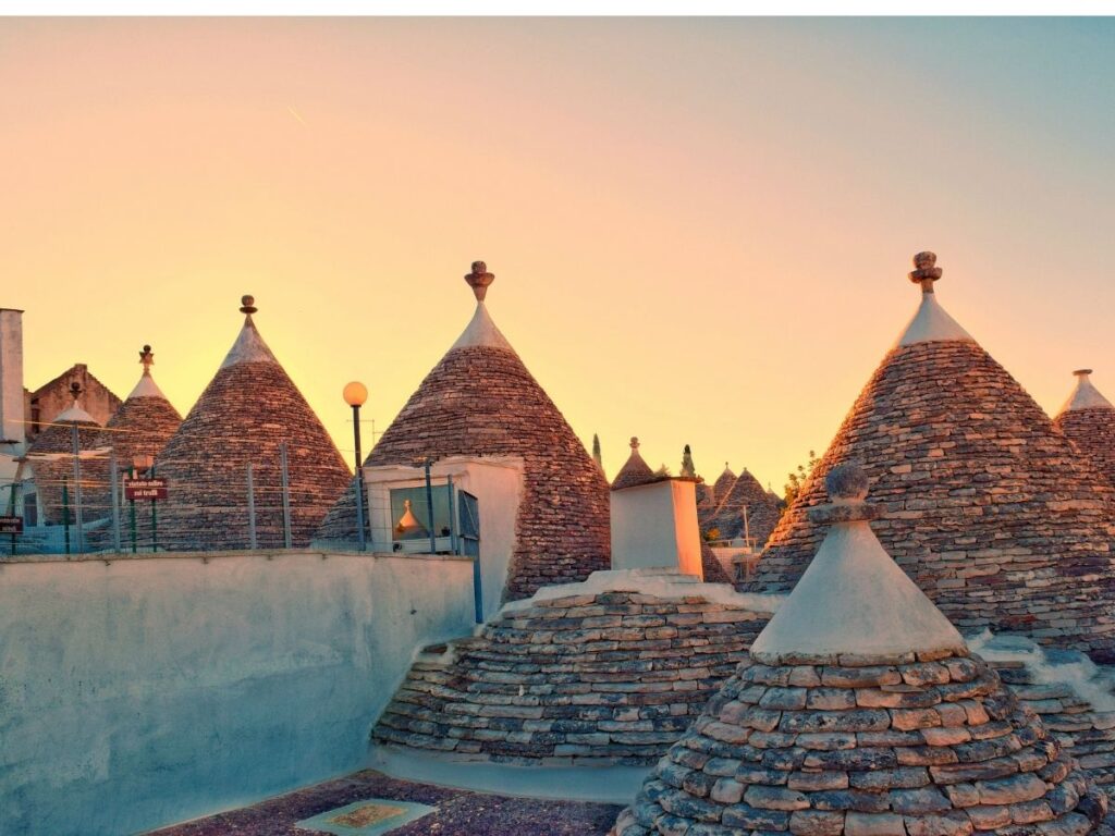 Trulli houses in Alberobello glowing at sunrise with empty cobblestone streets.