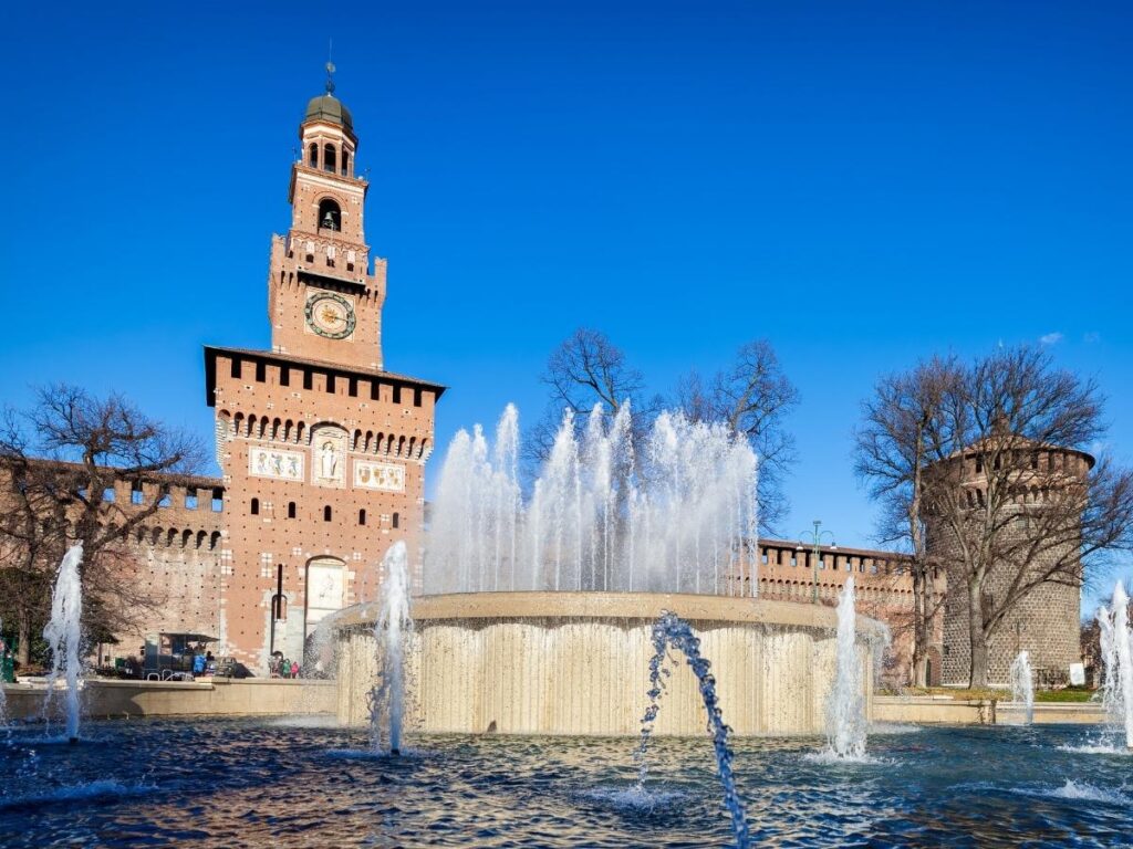 Red brick courtyard of Castello Sforzesco with Parco Sempione trees beyond.