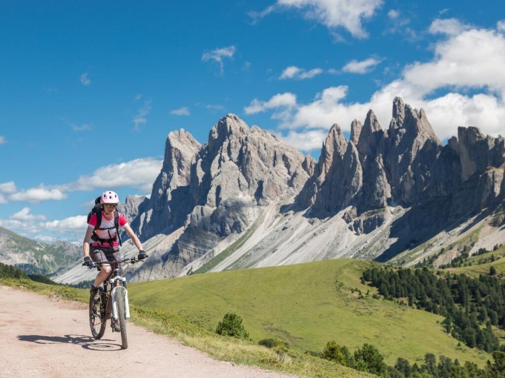 Cyclist riding through a winding mountain pass with Dolomite peaks in the distance.