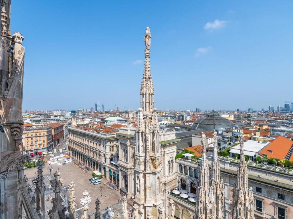 View from the Duomo rooftop showing marble spires and Milan skyline with distant Alps.