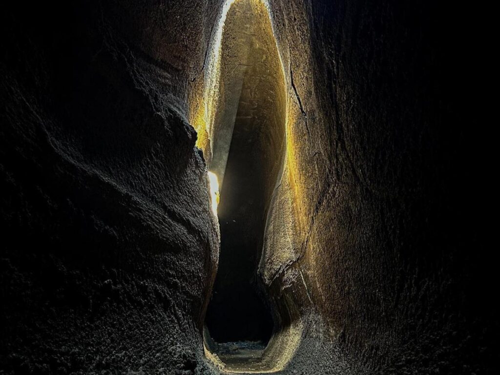Inside Grotta del Gelo lava cave, with permanent ice glistening against dark volcanic rock