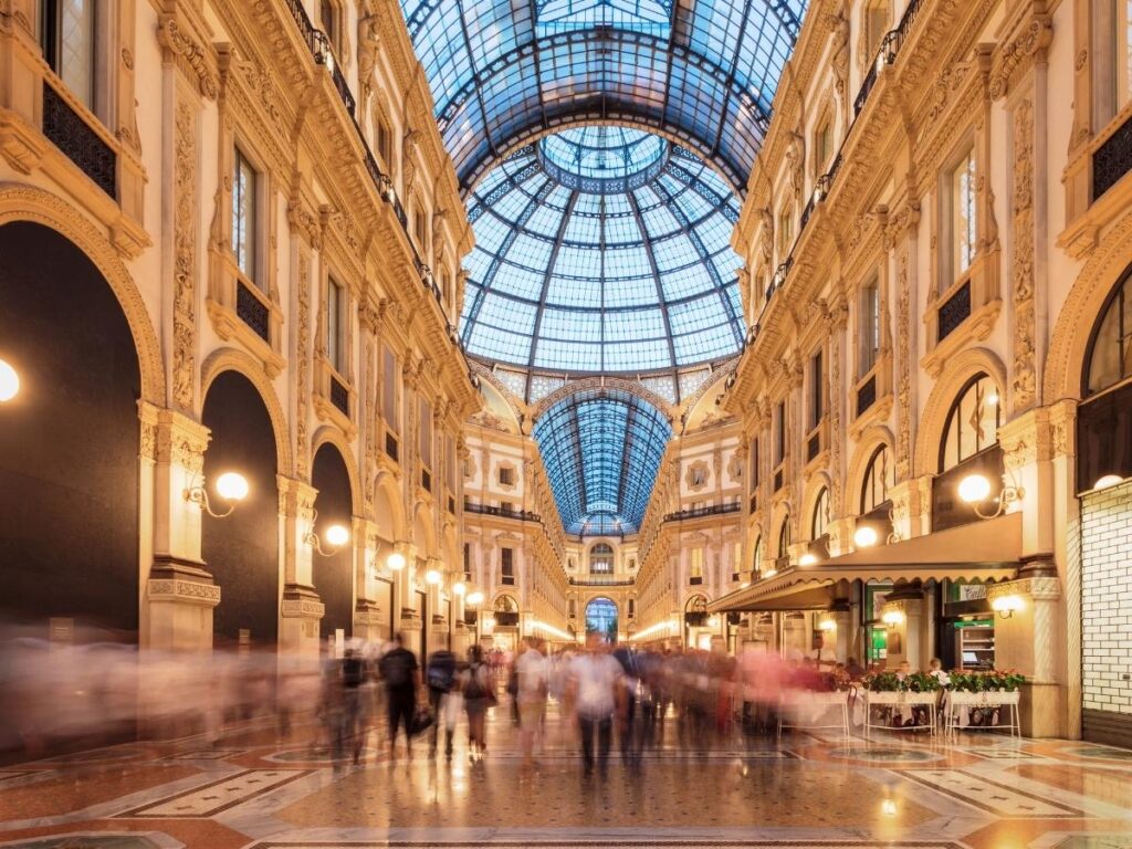Light streaming into Galleria Vittorio Emanuele II with people walking and cafés.