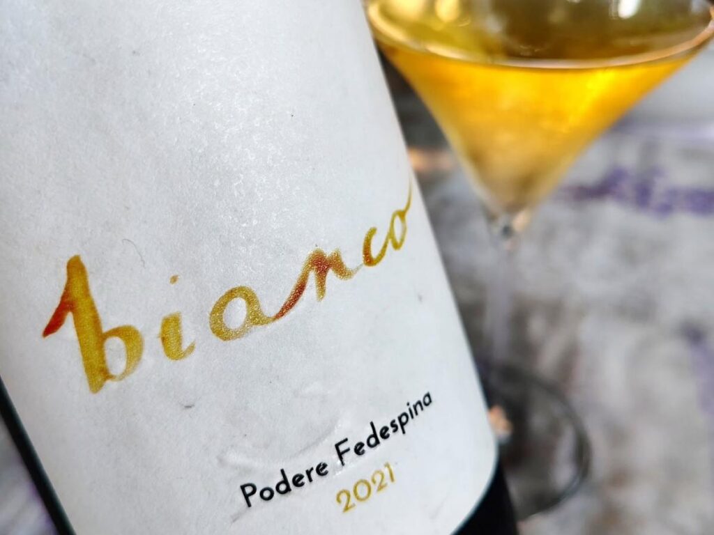 Bottle and glass of Greco di Bianco dessert wine with golden color.