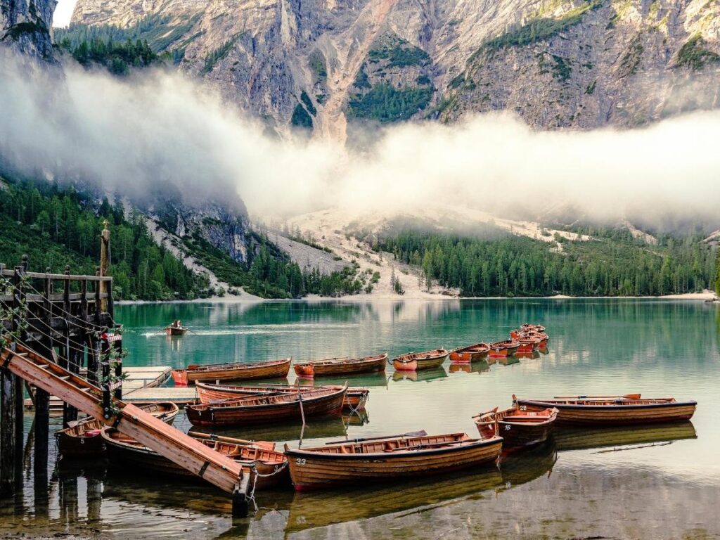 Wooden rowboats tied at the shore of Lago di Braies with turquoise water and pine-covered mountains reflected on the surface.