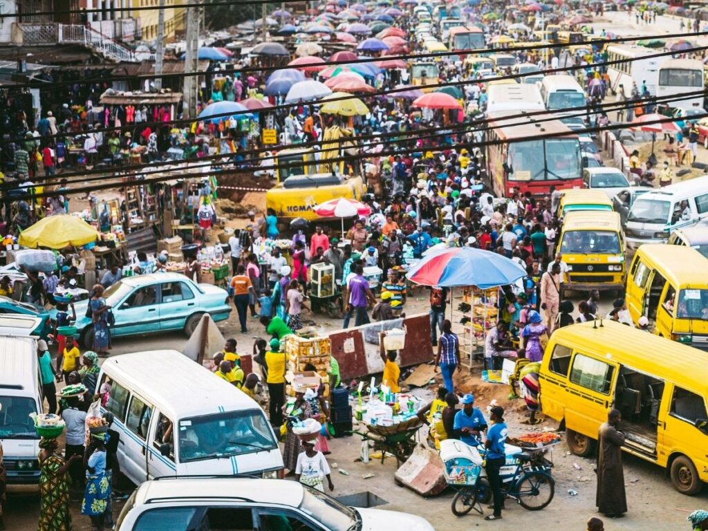 Pedestrians navigating dirt paths beside traffic in Lagos