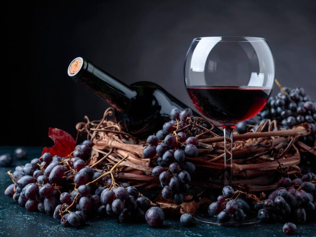 Glasses of sparkling red Lambrusco wine on a wooden table overlooking Modena vineyards at sunset.
