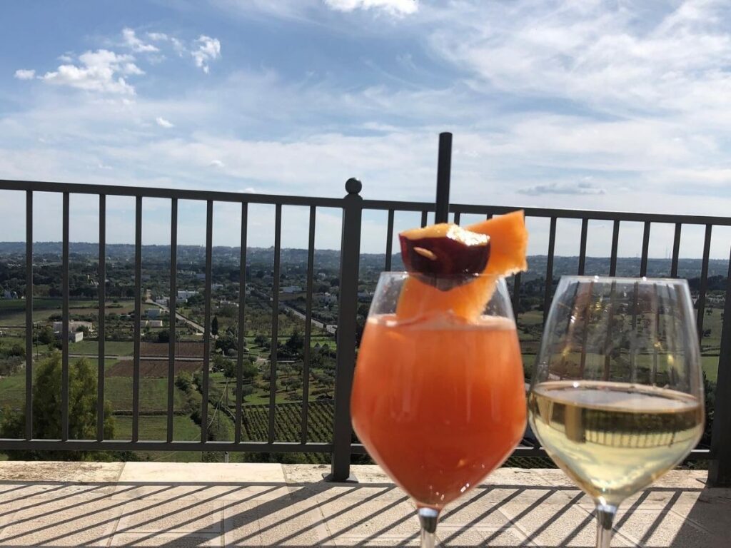 Glass of Locorotondo DOC wine at a viewpoint overlooking vineyards and olive groves.