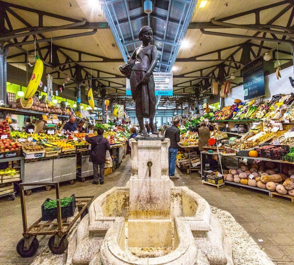 A bustling stall at Mercato Albinelli featuring Parmigiano Reggiano and fresh produce in Modena