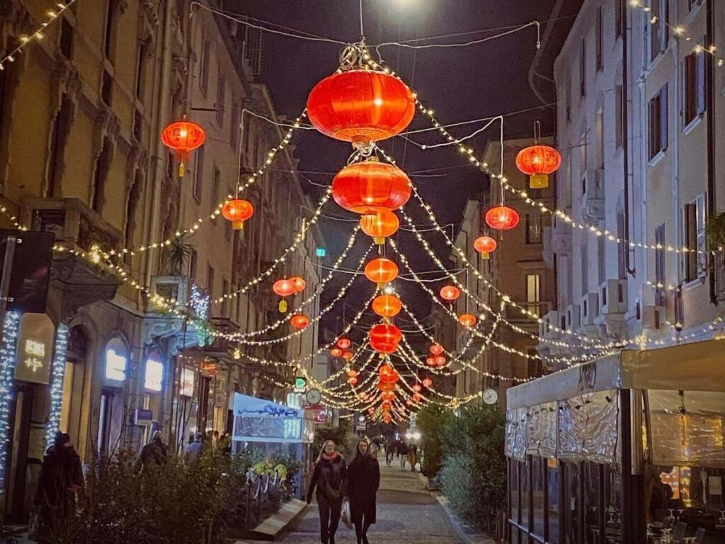 Busy street market in Milan’s Chinatown with food stalls and shoppers.